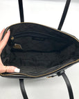 Black quilted handbag with gold zipper being held open by a hand on a white background