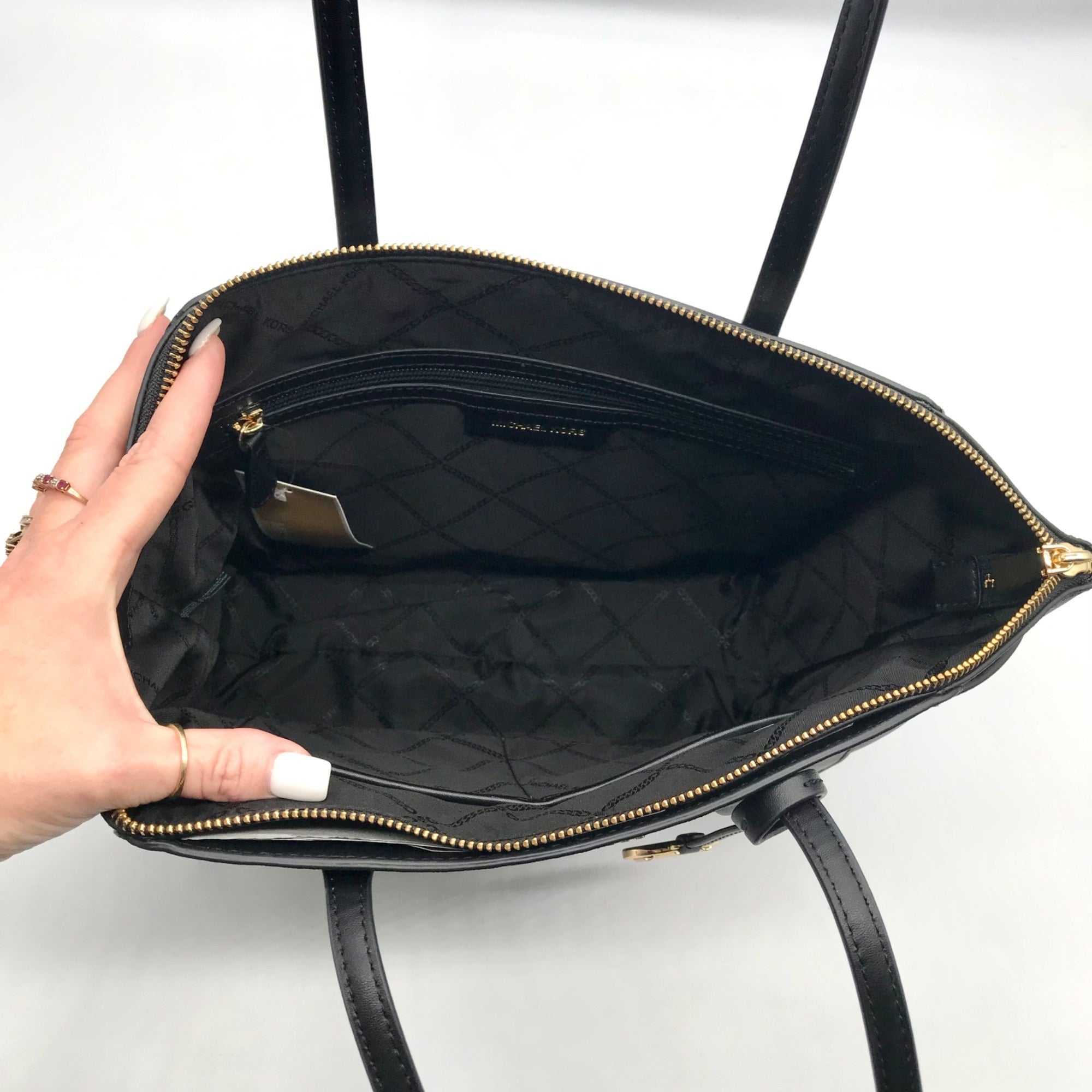 Black quilted handbag with gold zipper being held open by a hand on a white background