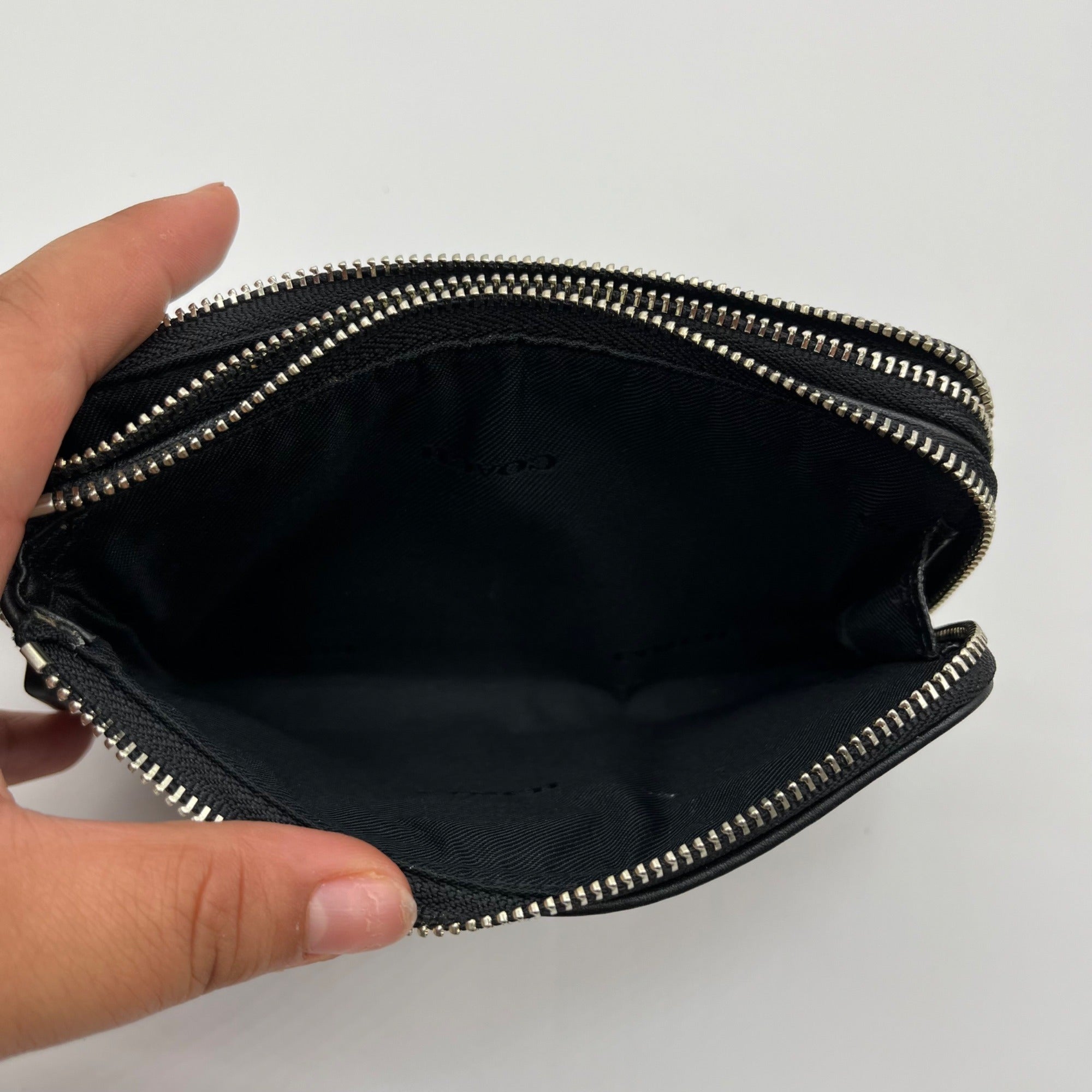 Black zippered pouch held open by a hand on a white background